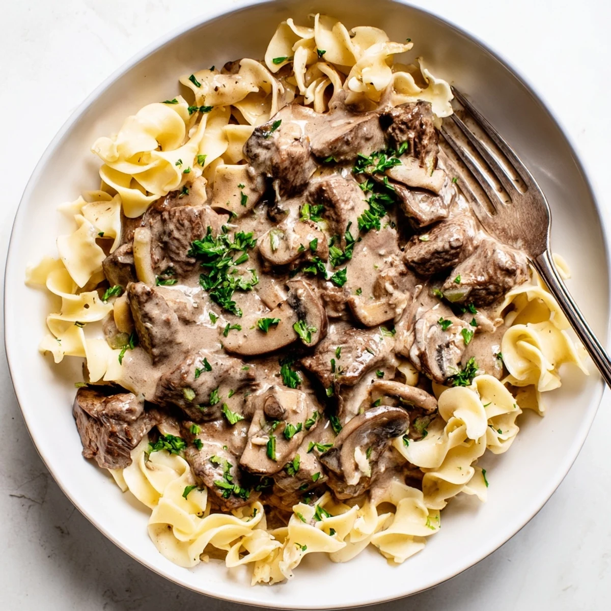 Savory easy beef stroganoff garnished with fresh parsley on a white plate.  