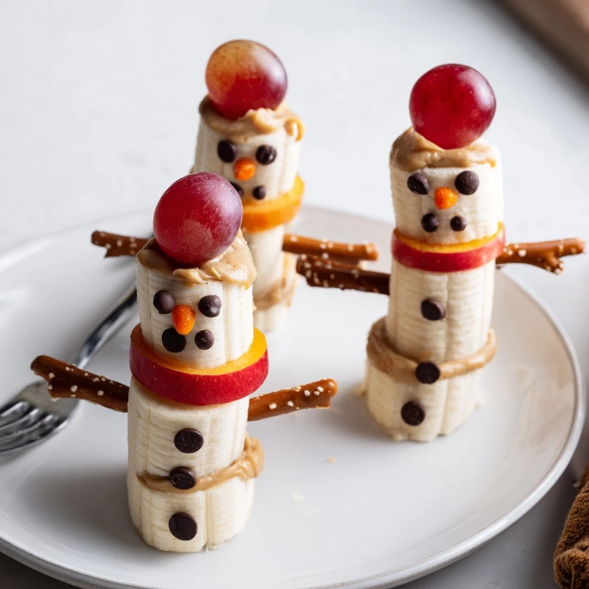 Adorable Banana Peanut Butter Snowmen snack arranged on a plate with pretzel arms, ready to eat.