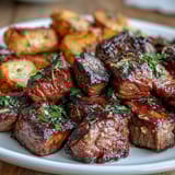 Tender sirloin steak bites and roasted baby potatoes tossed in a fragrant garlic butter sauce, garnished with fresh parsley and lemon zest.  