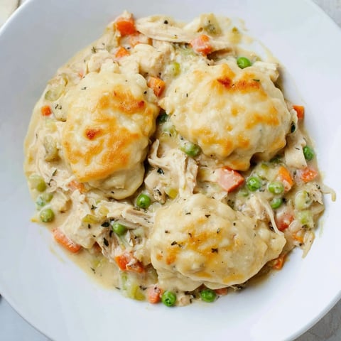 Golden-brown Chicken and Dumplings Casserole bubbling inside a baking dish, ready to serve with fragrant herbs.