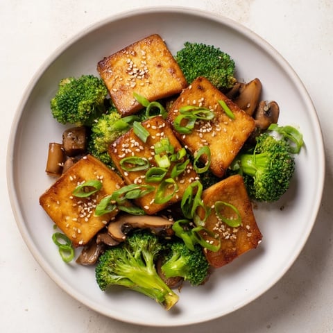 Vibrant image of golden sautéed tofu steak, broccoli, and mushrooms coated in savory sauce.