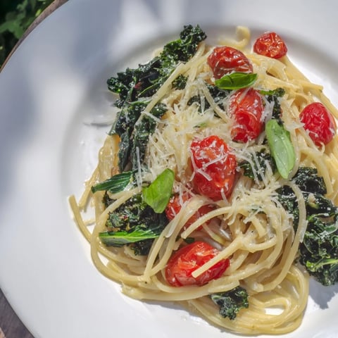 Steaming one-pot spaghetti with kale and tomatoes, garnished with fresh basil, ready to eat.