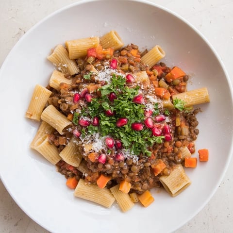 Steaming hot bowl of High-Fiber Lentil Bolognese Cozy Christmas Pasta, garnished with fresh parsley and pomegranate seeds.