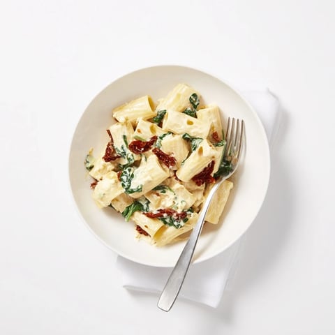 A bowl of Creamy Sun-Dried Tomato Spinach Cottage Cheese Pasta, garnished with fresh basil.