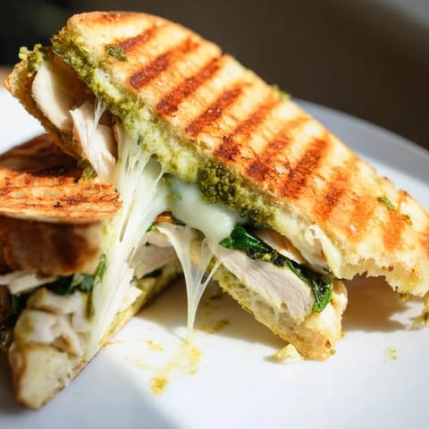 Freshly pressed Chicken Pesto Panini with juicy sliced chicken, gooey mozzarella, and basil pesto on toasty ciabatta bread.