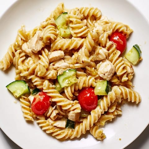 Colorful Honey Mustard Chicken Pasta Salad with fresh cherry tomatoes, cucumber, red bell pepper, and herbs served in a white bowl.  