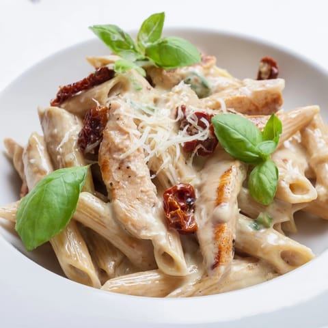 A close-up of Creamy Sun-Dried Tomato Chicken Pasta garnished with fresh basil, sun-dried tomatoes, and extra Parmesan cheese.
