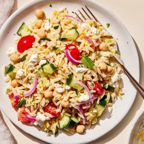 A vibrant bowl of Lemony Chickpea Orzo Salad with crisp cucumber, cherry tomatoes, and fresh parsley on a rustic table.