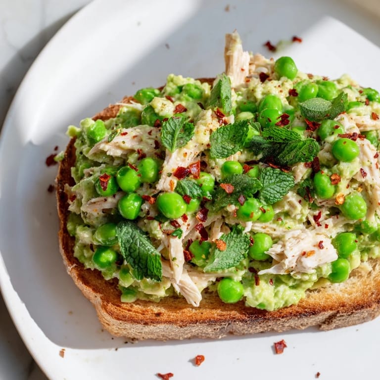 A vibrant Smashed Pea & Chicken Toast with fresh herbs and feta, served on a rustic plate.