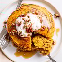 Golden-brown Pumpkin Spice Pancakes stacked high, drizzled with warm maple syrup and dusted with powdered sugar for a cozy autumn breakfast.