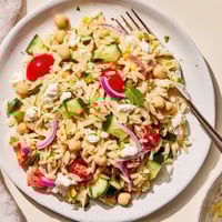 A vibrant bowl of Lemony Chickpea Orzo Salad with crisp cucumber, cherry tomatoes, and fresh parsley on a rustic table.